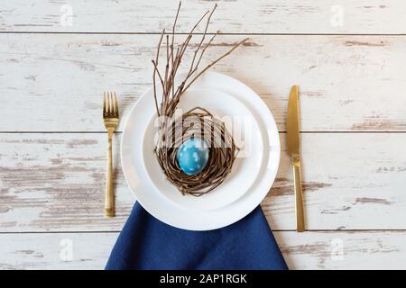 Creative festive Easter table setting on wood background with blue marble colored egg on a nest. Happy Easter time. Stock Photo