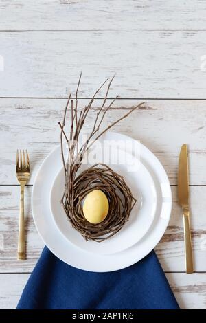 Creative festive Easter table setting on wood background with yellow egg on a nest. Happy Easter time. Stock Photo