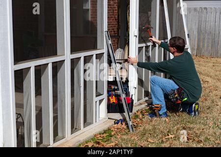 Man uses hammer to repair door on back porch Stock Photo