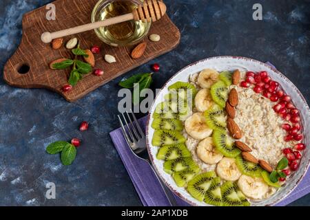 Breakfast consisting of oatmeal, nuts and fruits. Kiwi orange pomegranate almonds bananas decorate a plate. Healthy eating, on a dark background. Copy Stock Photo