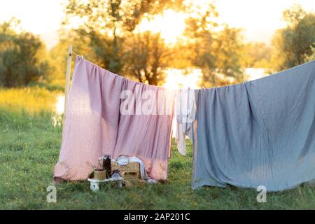 Pink and blue bedding sheet on forest background under the bright warm sun. Clean bed sheet hanging on clothesline at backyard. Hygiene sleeping ware concept. Stock Photo