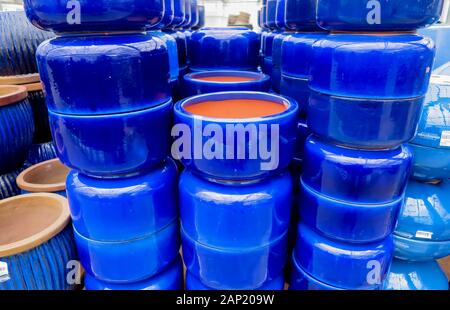 View on stapled pile of terra cotta flower pots painted in shiny vibrant blue color in german garden center Stock Photo