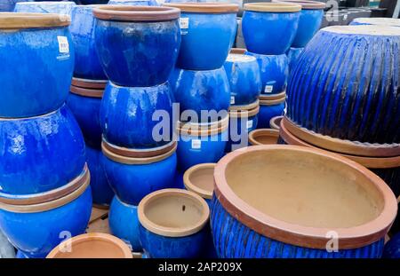 View on stapled pile of terra cotta flower pots painted in shiny vibrant blue color in german garden center Stock Photo