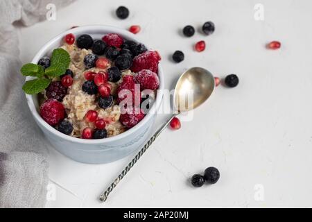 Breakfast consisting of oatmeal, nuts and fruits. Kiwi raspberries blackberries pomegranates almonds mint decorate a plate. Healthy eating, on a light Stock Photo