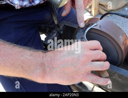 knife sharpener sharpens the blade of a bill hook using a grinding wheel Stock Photo