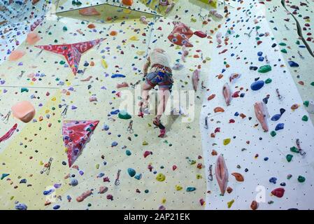 Man climbing wall in bouldering gym. Detail on legs and equipment