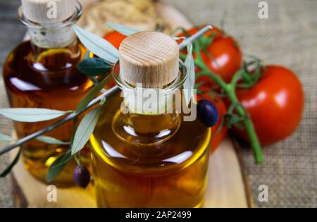 Mediterranean italian healthy food concept: isolated close up of olive oil bottles on wood cutting board with twig and red tomatoes Stock Photo