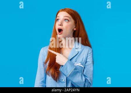Omg check it out. Startled and emotional impressed redhead female drop jaw, staring upper left corner with amazed expression, popping eyes at Stock Photo