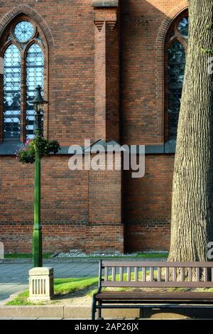 Fragment of a red brick wall with a window with an arch, with a bench in the foreground. Stock Photo