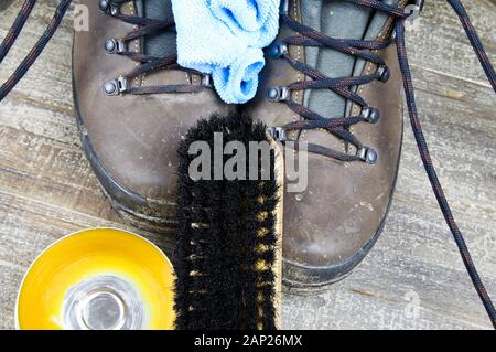 Cleaning brown dirty leather boots: Shoes, box with shoe wax, blue cloth and black brush on wood table Stock Photo