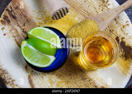 Receipt and preparation of caipirinha cocktail: Close up of glass with Cachaça, wooden plunger, sliced limes and spoon with brown sugar Stock Photo
