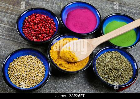 Close up view from above on six blue bowls with various colorful spice powder and grains on wood table. Spoon in turmeric curcuma bowl. Stock Photo