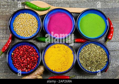 Close up view from above on six blue bowls with various colorful spice powder and grains on wood table. Stock Photo