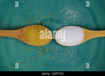Sugar comparison concept: Close up of two isolated wood spoons with brown cane and white industrial refined sugar on green china dish Stock Photo