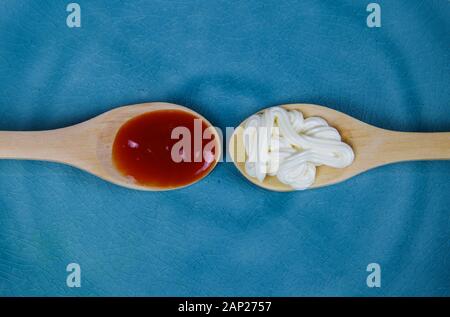 Close up of two isolated wood spoons with mayonnaise and red ketchup on blue chine plate Stock Photo