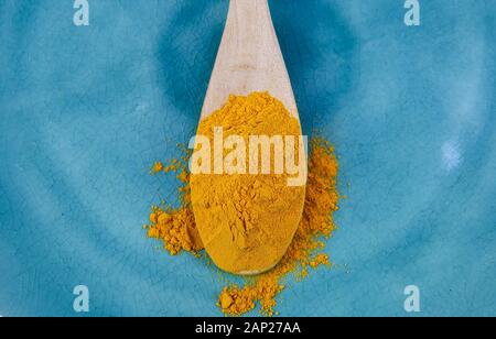 Close up of isolated wood spoon with yellow curcuma powder on blue old scratched china dish Stock Photo