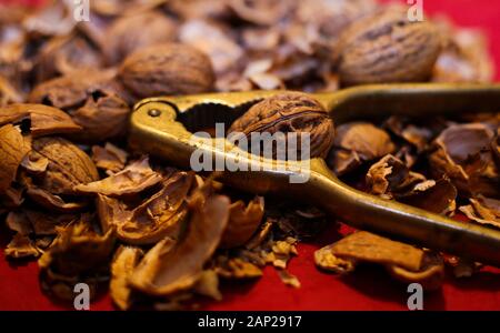 Close up pile with cracked walnut shells and isolated retro lever nutcracker with red background. Stock Photo