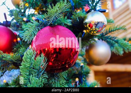 Close up of Christmas tree branch with red and silver balls decoration. Blurred wood house background on Christmas market Stock Photo