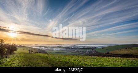 Panoramic View from hilltop of sun setting over valley shrouded in mist in Dorset, UK Stock Photo