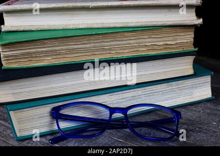 View on isolated stack of old yellowed books on wood table with blue reading glasses Stock Photo