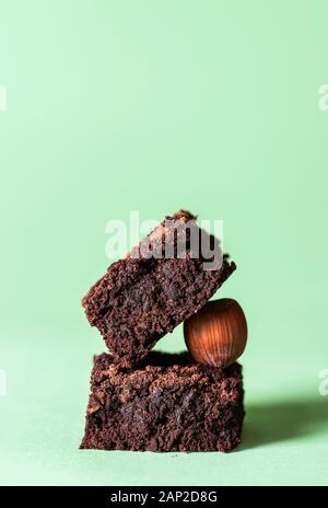 Stack of two dark chocolate brownies and a hazelnut, on a mint green background. Delicious fudge chocolate cake squares. A cute pile of brownies. Stock Photo