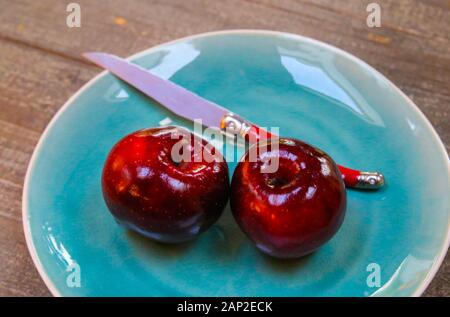 Close up of isolated two red dotted shiny isolated dessert apples on blue china dish with knife Stock Photo