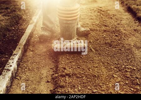 Stamping soil with rammer to build the garden path in the evening sunshine Stock Photo