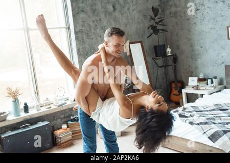 Mixed Race Couple. Young man holding woman's hip dancing in bedroom smiling playful having fun Stock Photo