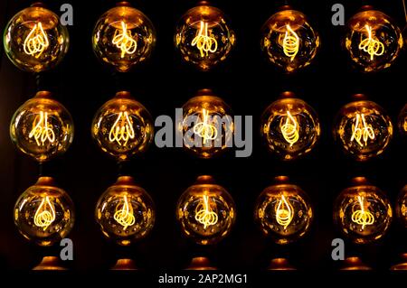 Isolated group of yellow gold shining retro classical light bulbs in rows with glowing filaments and black background Stock Photo