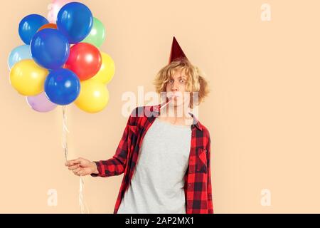 Young man holding helium balloons, blowing in party horn Stock Photo
