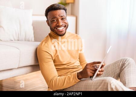 Afro Man Using Tablet Smiling Sitting On Floor At Home Stock Photo
