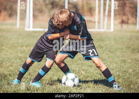 Boys in soccer jerseys kicking football on the sports field Stock Photo