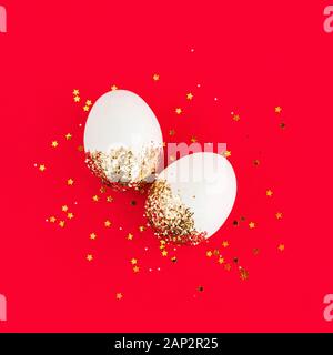 White easter eggs in golden glitter confetti and stars on red background and copy space. Square. Stock Photo