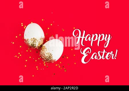 White easter eggs in golden glitter confetti and stars on red background and words Happy easter. Top view. Stock Photo