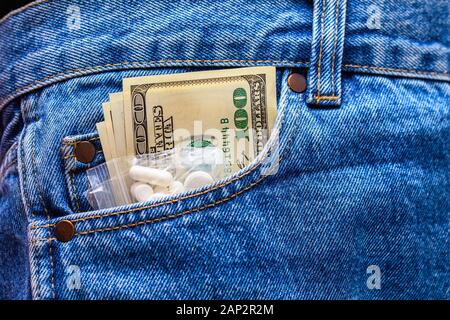 White drug pills and US dollar banknotes in the pocket of jeans. Concept of med expenses or illegal drug distribution. Stock Photo