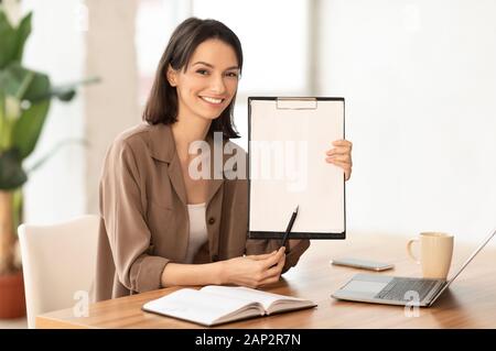 Smiling woman showing blank clipboard at office Stock Photo