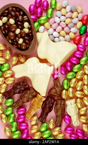 Happy Easter creative layout flat lay display of an assortment of white, milk and dark chocolate and candy rabbits, bunnies and eggs on pink backgroun Stock Photo