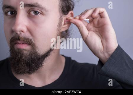 portrait of a young bearded guy. Close-up of a man using a cotton swab to clean sulfur in his ears. Ear health, care and cleaning. Perforation of the Stock Photo