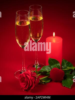 red rose, two glasses of champagne, a lit candle and a red heart on a red background in honor of Valentine's day, wedding day, anniversary. Stock Photo