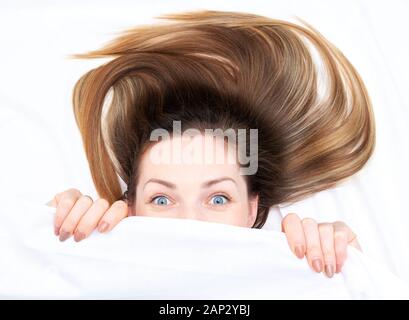 Amazing girl with open eyes looking out from under the covers Stock Photo
