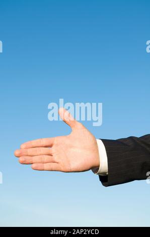 Hand of a businessman outstretched for a handshake outdoors in sunny blue sky Stock Photo