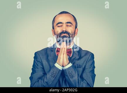 Closeup portrait of a mature middle-aged sad man praying eyes closed. Mixed race bearded model isolated on green yellow studio background with copy sp Stock Photo