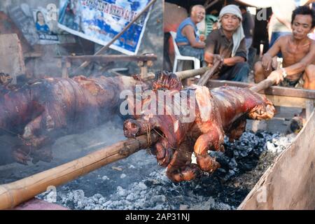 Spit roasted pig known as ‘Lechon Baboy’ in the Philippines being roasted over burning embers during the Sinulog Festival,Cebu City, Stock Photo