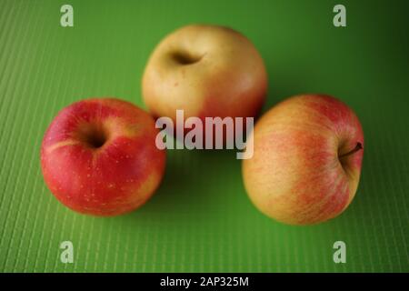 three ripe apples, red with yellow color, lie on a green table. Stock Photo