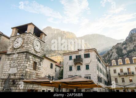 Morning sunlight hits the mountains above the Clock Tower in the Piazza of the Arms, the main and largest town square in Kotor, Montenegro Stock Photo