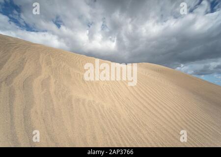 Golden ridges of the Maspalomas Dunes sculpted by Atlantic winds,creating an endless desert-like landscape bathed in dramatic stormy skies over island. Stock Photo
