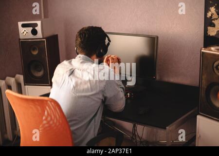 Concentrated man in headphones sitting by desktop computer Stock Photo