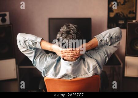 Man relaxing sitting on chair by computer with hands behind head Stock Photo