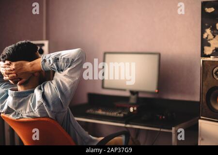 Man relaxing sitting on chair by computer with hands behind head Stock Photo