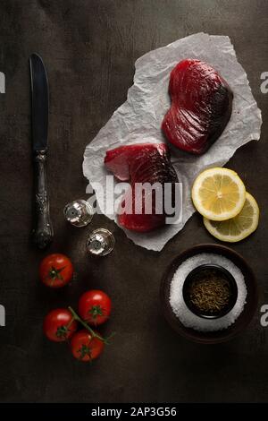 Yellowfin tuna slices on a dark background with carrots, salt, pepper, knife and many other ingredients Stock Photo